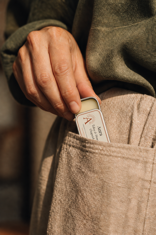 A hand placing an Aura-labelled silver chapstick tin into a linen pocket